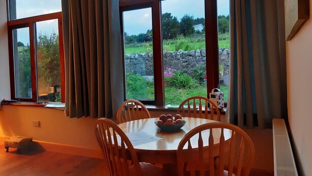Ein Essbereich mit Tisch und Stühlen, einer Obstschale und Blick auf einen Garten durch große Fenster.