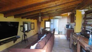 A cozy living room with a wooden ceiling, a large flat-screen TV, a leather sofa, and a dining area with a table and chairs.