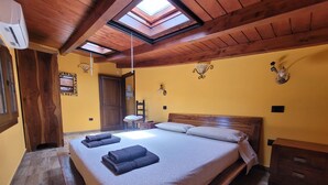 A bedroom with a large bed, wooden ceiling beams, a skylight, and a wooden wardrobe.
