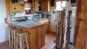 A kitchen with wooden cabinets, a tiled backsplash, hanging pots, stools, and a stainless steel refrigerator. - Glamping, off-grid adventure at peace-friendly cabin on 10 acres w/ STARGAZING! (Fredonia)