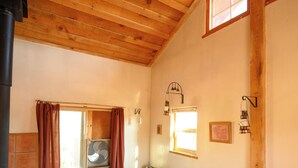 A cozy living room with a wooden ceiling, a leather sofa, a wooden table, and a window with curtains. - Glamping, off-grid adventure at peace-friendly cabin on 10 acres w/ STARGAZING! (Fredonia)