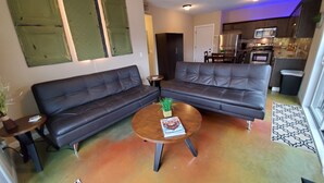 A living room with a black leather sofa, a coffee table with magazines, and a kitchen in the background. - 9th St. Beals Loft Downtown Columbia (Columbia)