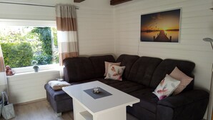A living room with a dark brown sofa, a white coffee table, and a window with curtains. - Idyllic holiday home on the forest and lake in Klingberg (Klingberg)