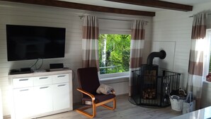 A living room with a TV, a wooden cabinet, a rocking chair, a fireplace, and a window with curtains. - Idyllic holiday home on the forest and lake in Klingberg (Klingberg)