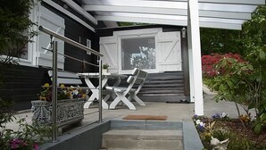 A modern outdoor seating area with a metal railing, a staircase leading to a covered entrance, and a variety of potted plants. - Idyllic holiday home on the forest and lake in Klingberg (Klingberg)