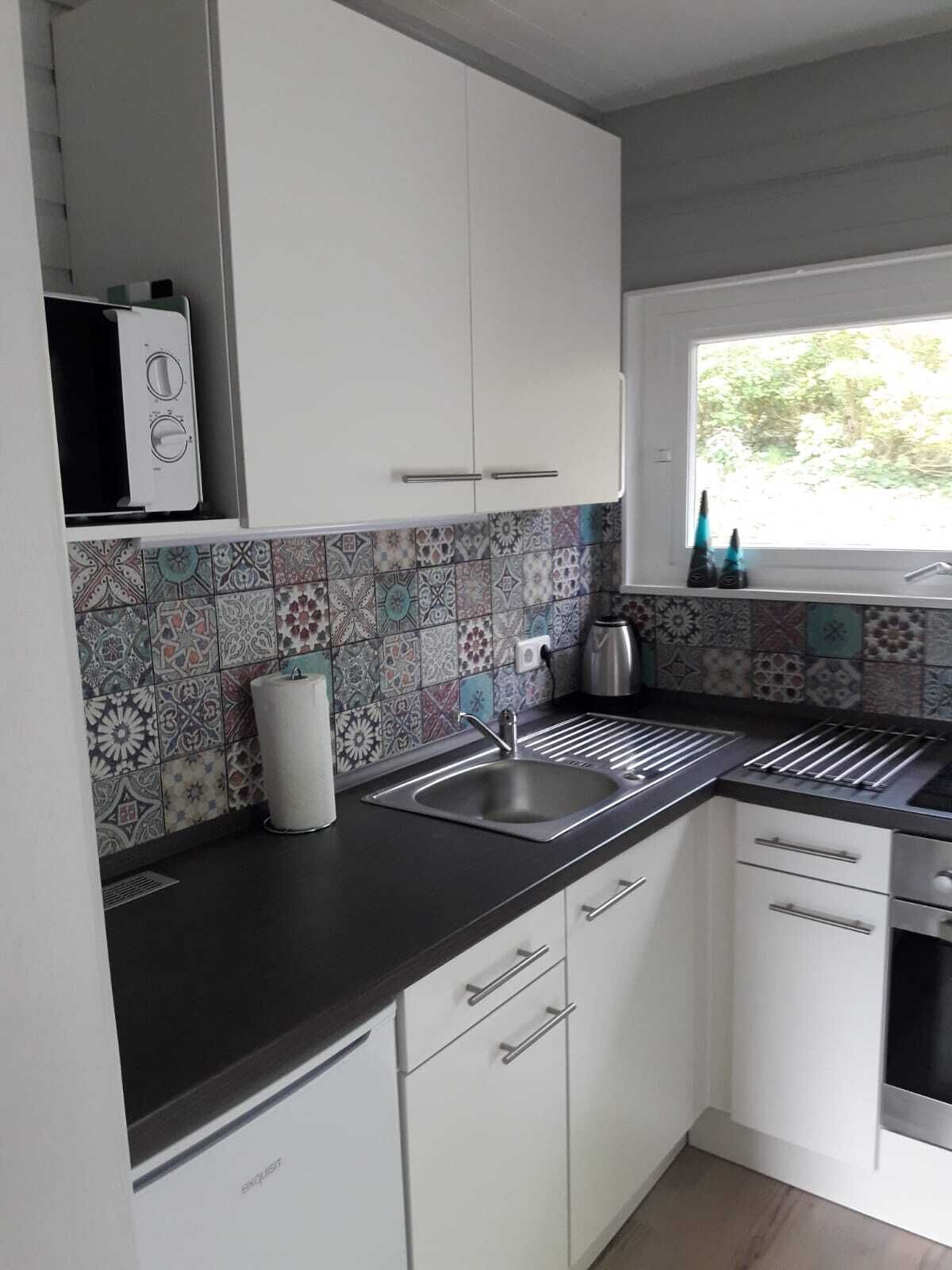 A modern kitchen with white cabinets, a patterned backsplash, a stainless steel sink, and a window with a view of greenery.