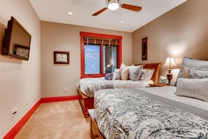 A bedroom with two beds, a window with a view, a ceiling fan, and a clock on the wall.