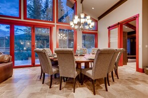 A dining area with a large table, six upholstered chairs, and a chandelier.
