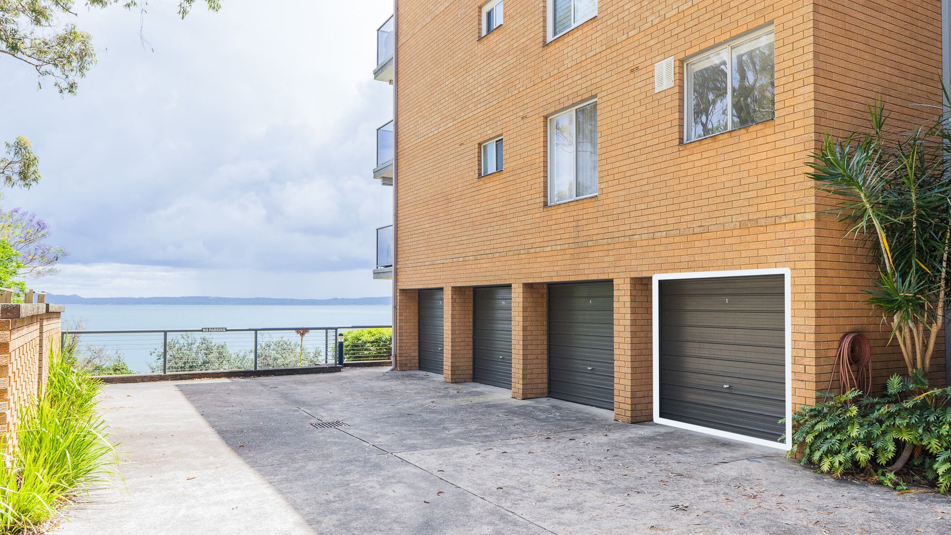 A multi-story building with a brick facade, a concrete ground floor, and a view of a body of water.