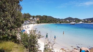 Une plage avec une eau claire, des gens qui se baignent et des bâtiments en arrière-plan.