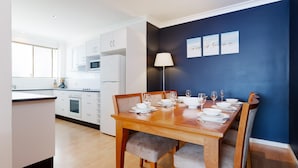 Une cuisine moderne avec des meubles blancs et un coin repas doté d’une table en bois, mise pour quatre personnes.