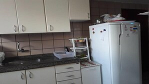 Keitti össä on valkoiset kaapit, graniittitaso, valkoinen jääkaappi, jossa on magneetteja, ja hedelmäkori.
