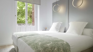 A modern bedroom with a large bed, two bedside tables, and a window with a view of greenery. - Avenida Suite by FeelFree Rentals (San Sebastián)