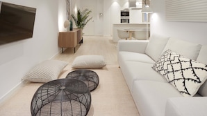 A modern living room with a white sofa, two black round tables, and a TV on the wall. - Avenida Suite by FeelFree Rentals (San Sebastián)