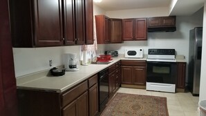 A kitchen with dark wooden cabinets, a white countertop, a coffee maker, a microwave, a stove, and a refrigerator. - Beautiful 3 Bedroom House Close To Richmond Raceway (Richmond)