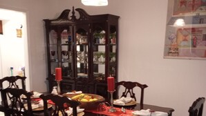 A dining area with a wooden table, chairs, a red candle, and a dark wooden cabinet with glass doors. - Beautiful 3 Bedroom House Close To Richmond Raceway (Richmond)