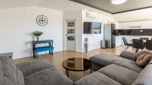 Una sala moderna con un sofá, una mesa de centro y un banco azul. Se observa una cocina al fondo con un televisor montado en la pared.
