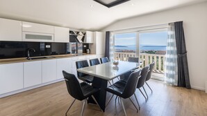 Una cocina moderna con armarios blancos, encimera negra y un comedor con mesa de vidrio y sillas negras.