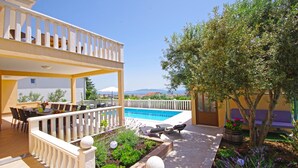 Zona de piscina con un espacio de estar cubierto, una piscina y un jardín con diversas plantas.