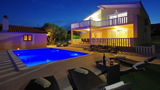 Una casa de dos pisos con piscina, mobiliario de exterior y un balcón.
