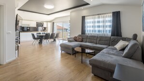 Una sala de estar moderna con un sofá seccional, una zona de comedor y una cocina al fondo.
