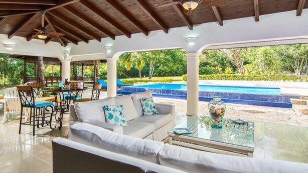 Eine Außenlounge mit Pool, weißer Möbel und Deckenventilator.