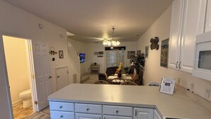 A kitchen with white cabinets, a central island, and a dining area in the background. -  Quiet Bethany Beach Condo   -  Pool • Tennis • Sleeps 8 • 2 Miles to Beach (Frankford)