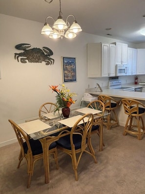Un coin repas avec une table en verre et des chaises en osier, un panneau décoratif représentant un crabe et un tableau encadré accroché au mur.