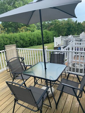 Une terrasse avec une table et des chaises en verre, une clôture blanche et une haie en arrière-plan.