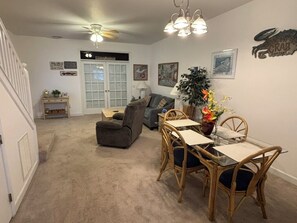 Un salon avec une table à manger en verre, des chaises en osier, un canapé gris et un ventilateur de plafond.