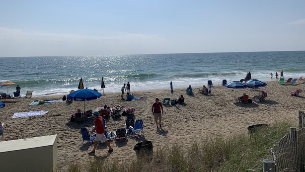 A beach with people relaxing under umbrellas, some walking along the shore, and beach chairs scattered around. -  Quiet Bethany Beach Condo   -  Pool • Tennis • Sleeps 8 • 2 Miles to Beach (Frankford)