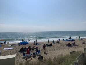 Une plage où l’on voit des gens se détendre sous des parasols, d’autres se promener le long du rivage, et des chaises de plage disposées un peu partout.