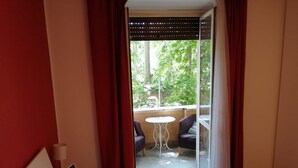 Une chambre d’hôtel avec un lit, une petite table, deux chaises et un balcon donnant sur la verdure.