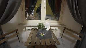 Une petite table en bois, sur laquelle se trouvent un pot de fleurs et un menu, est placée devant une fenêtre ornée de rideaux.