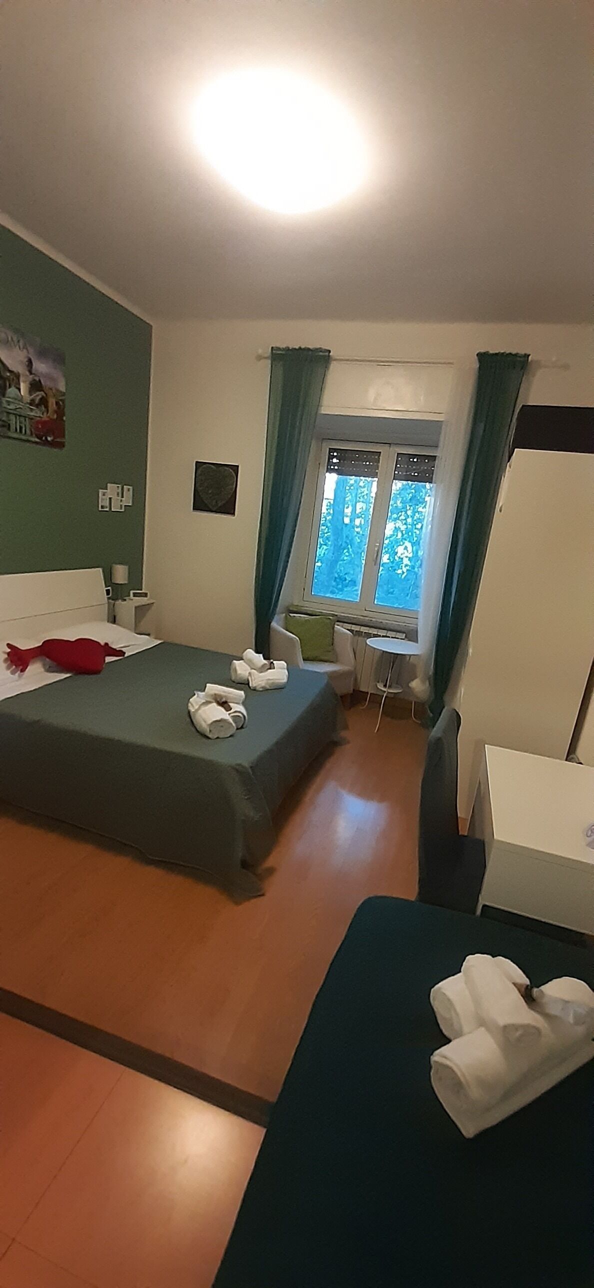 Ein Hotelzimmer mit Bett, Schreibtisch, Stuhl, einem Fenster mit Vorhängen und einem Bild an der Wand.