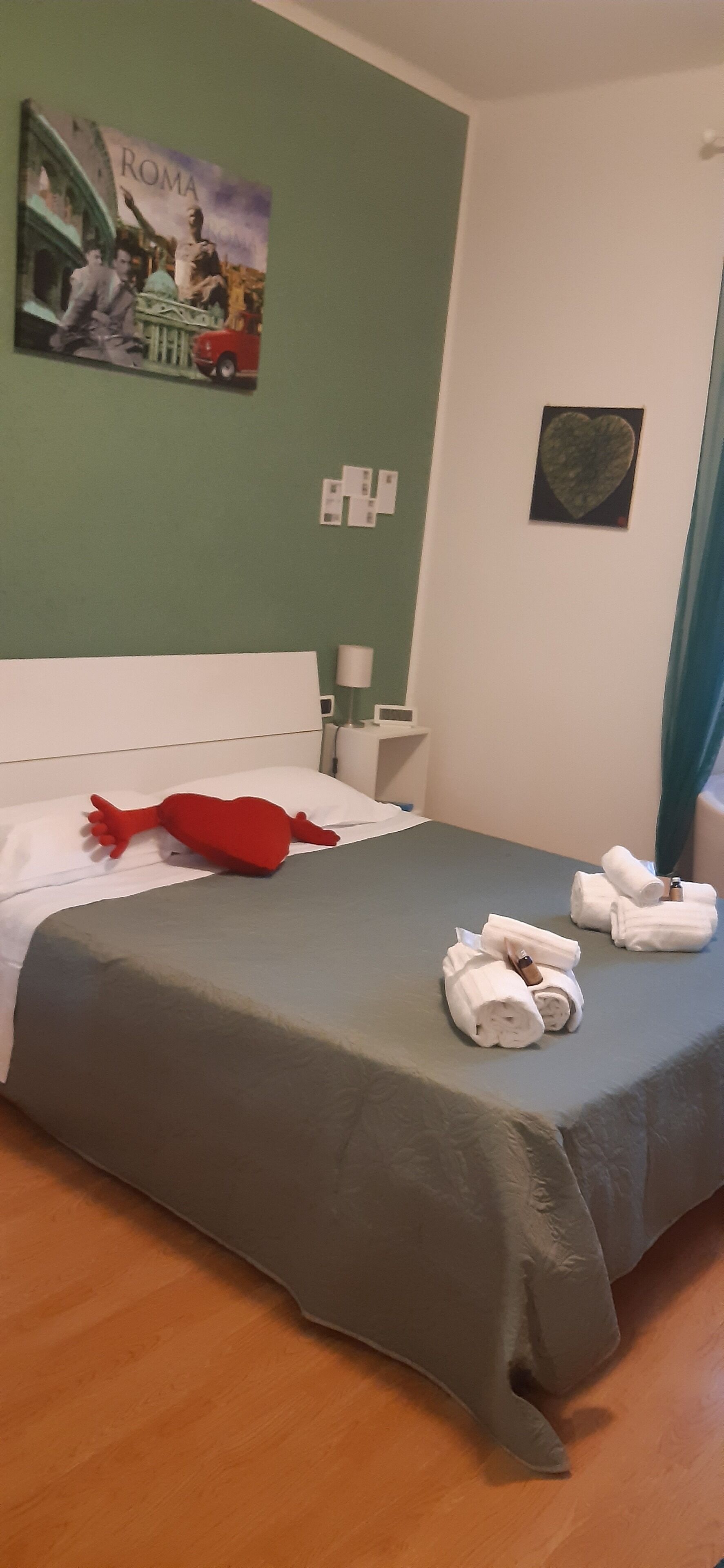 Un letto ben rifatto con una coperta grigia, un cuscino rosso e asciugamani arrotolati su un lato.