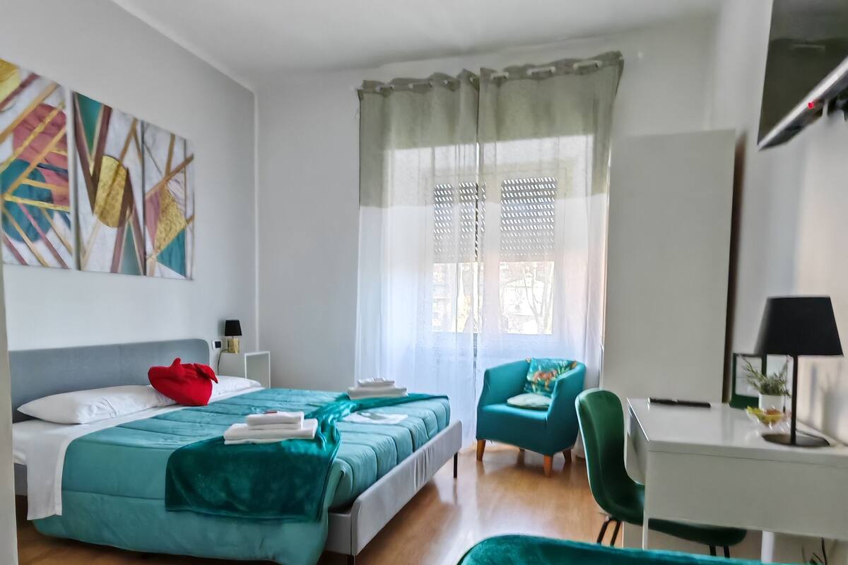 Habitación de hotel moderna con dos camas, un escritorio, una silla y un ventanal con cortinas.