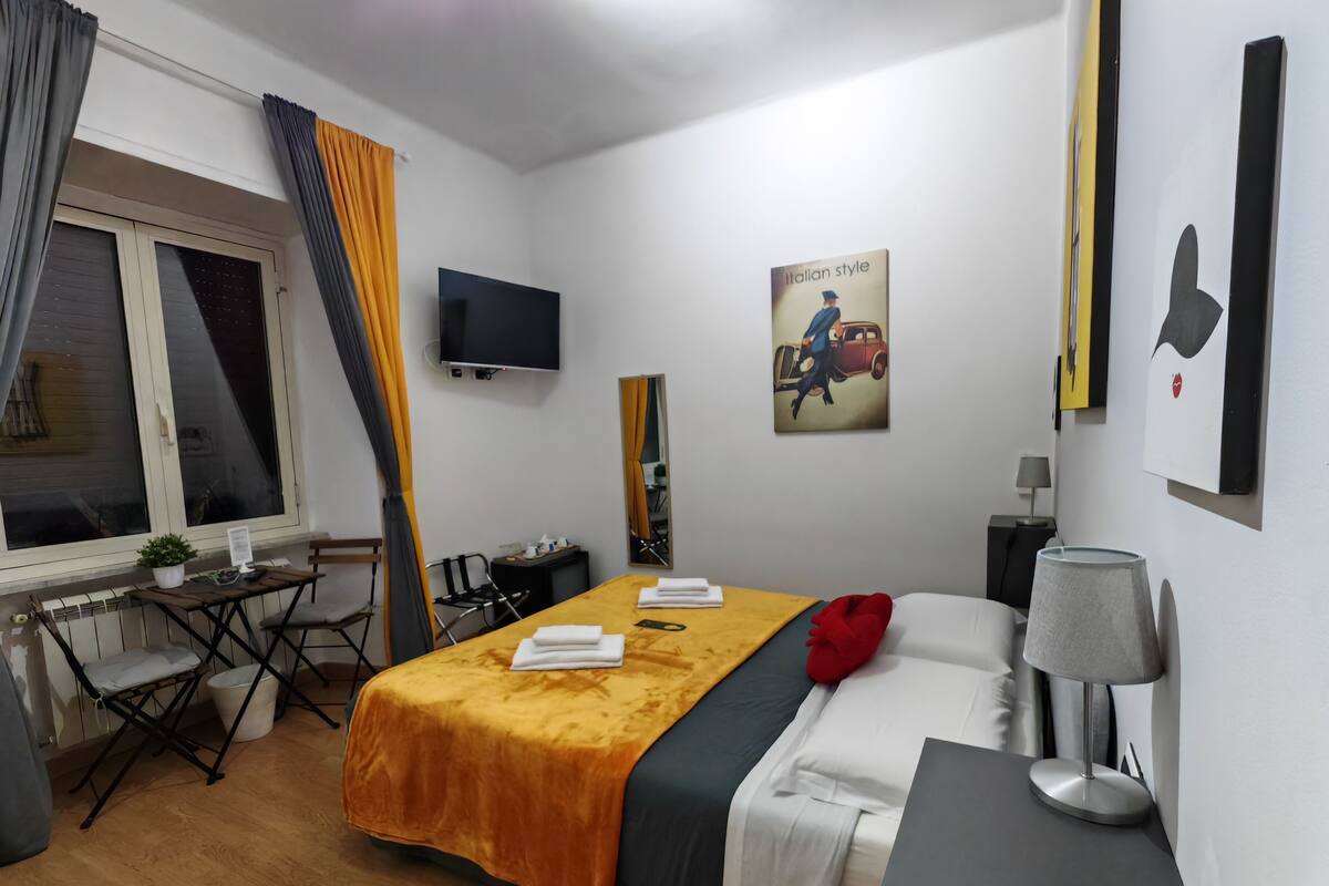 Una habitación de hotel con una cama, un escritorio, una silla, un televisor y un cuadro en la pared.