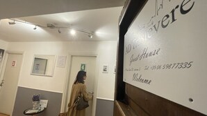 Un couloir avec une pancarte indiquant « AD L'INTERNATE, maison d’hôtes » et un numéro de téléphone. On y trouve les portes numérotées 3 et 4, ainsi qu’une petite table sur laquelle sont posés un vase et un livre.