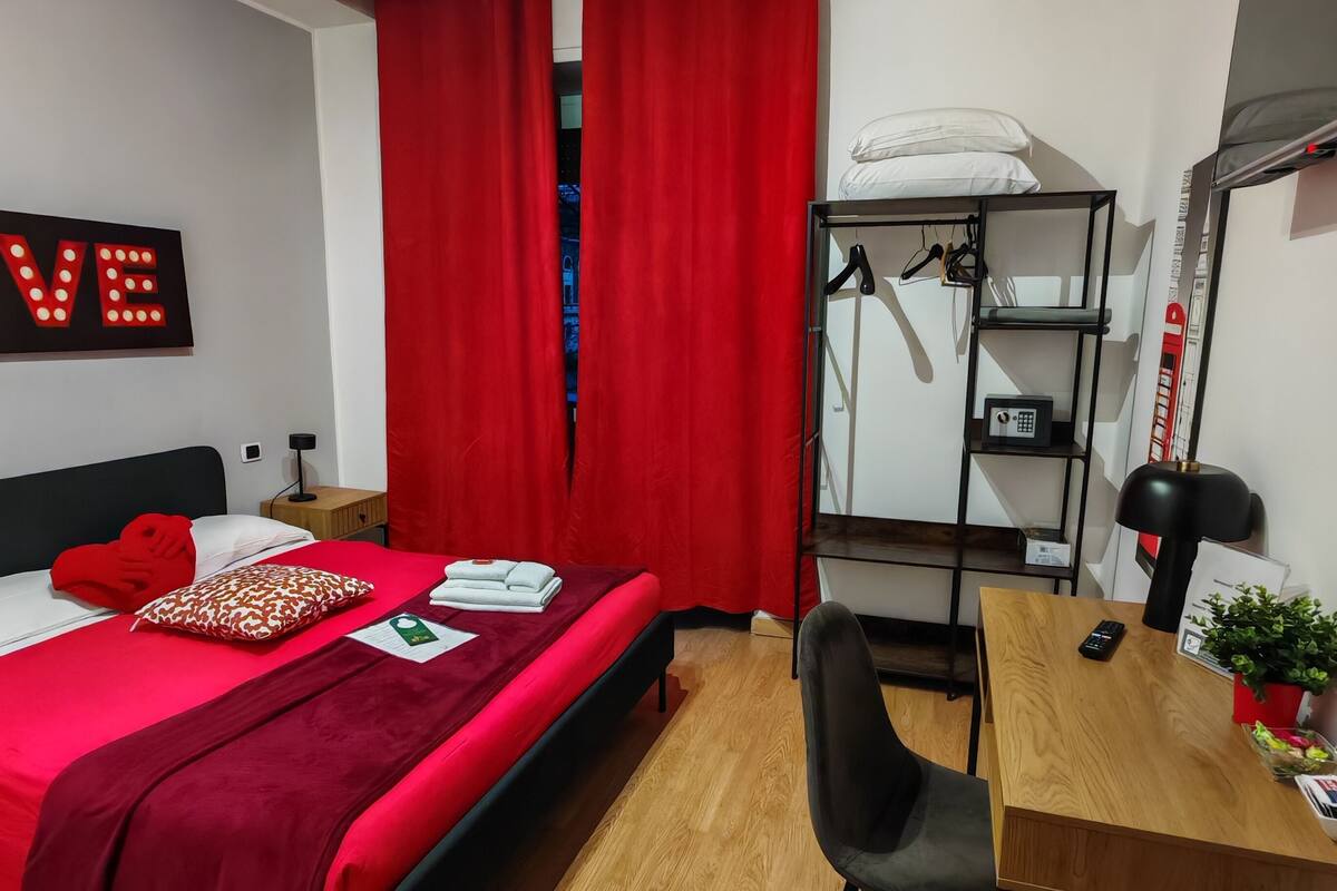 Una habitación de hotel moderna con una cama, un escritorio, una silla, un armario y una cortina roja.