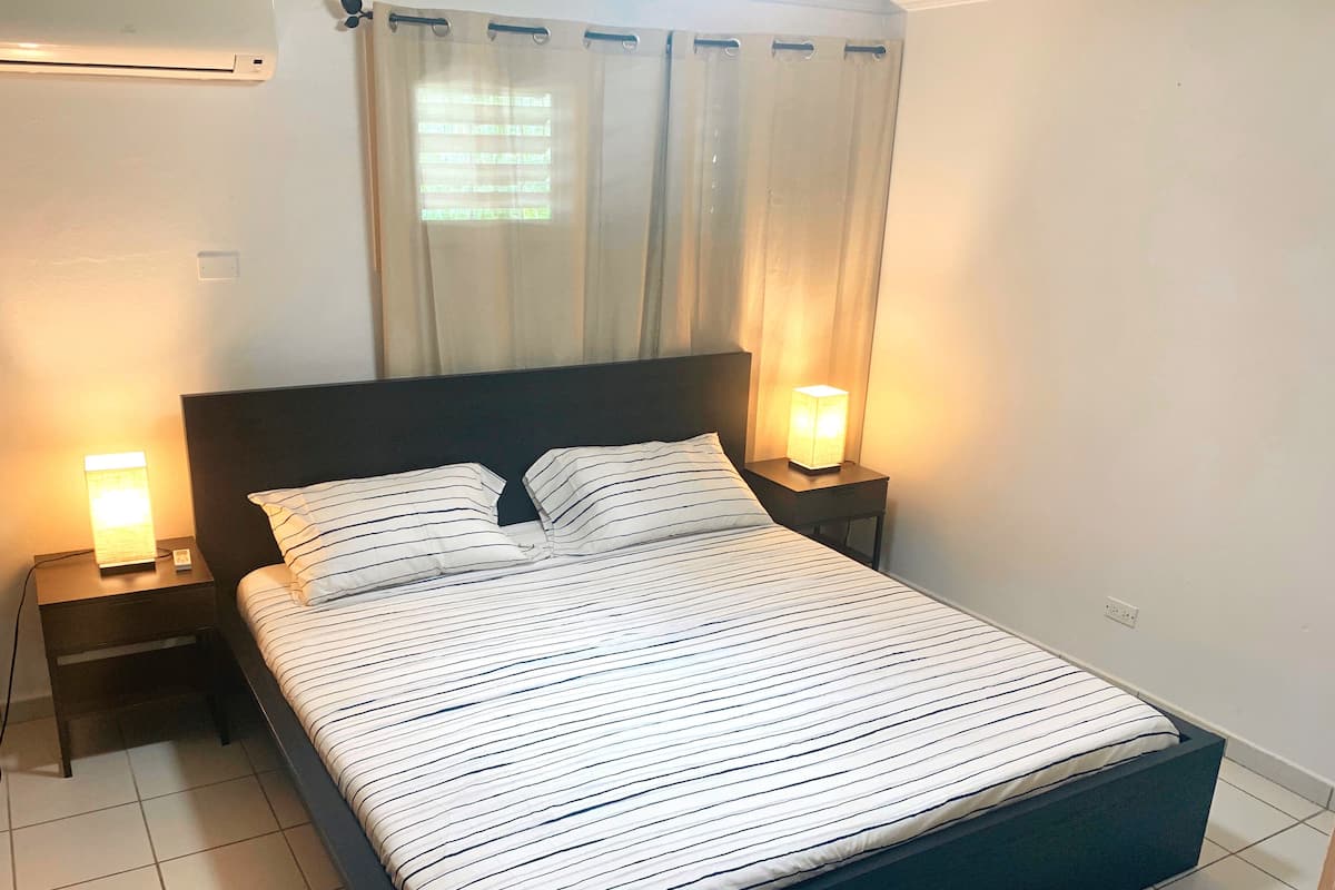 A bed with striped bedding, two bedside lamps, a nightstand, a headboard, and a window with curtains.