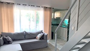 A living room with a grey sofa, a staircase leading to a kitchen, and a window with sheer curtains. - Cozy one-bedroom & mezzanine apartment (Philipsburg)