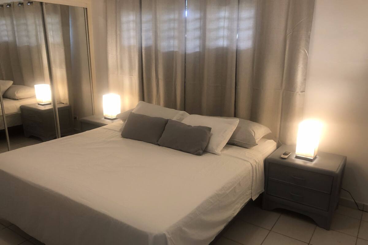 A neatly made bed with white linens and gray pillows, two bedside tables with lamps, and a large mirror on the wall.