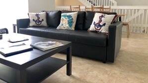 A living room with a black leather sofa, a wooden coffee table, and a staircase with white railings. - Home in Fort Lauderdale (Fort Lauderdale)