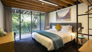 Une chambre d’hôtel moderne, dotée d’un grand lit, d’un bureau et offrant une vue sur la verdure par la fenêtre.