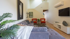 Un salon moderne avec un canapé gris, des fauteuils rouges, une table basse et un téléviseur fixé au mur.