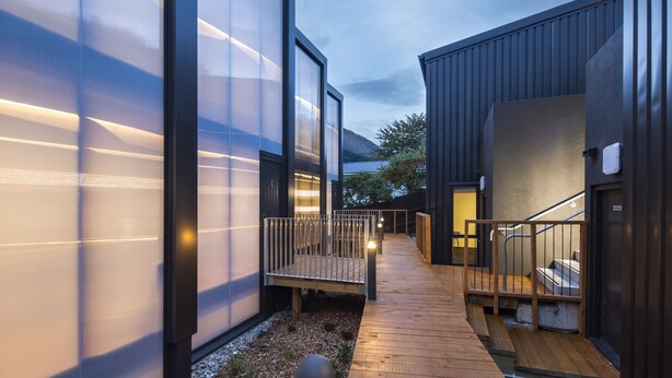 Un bâtiment moderne doté de grandes fenêtres en verre, d’une terrasse en bois et d’un escalier menant à un niveau supérieur.