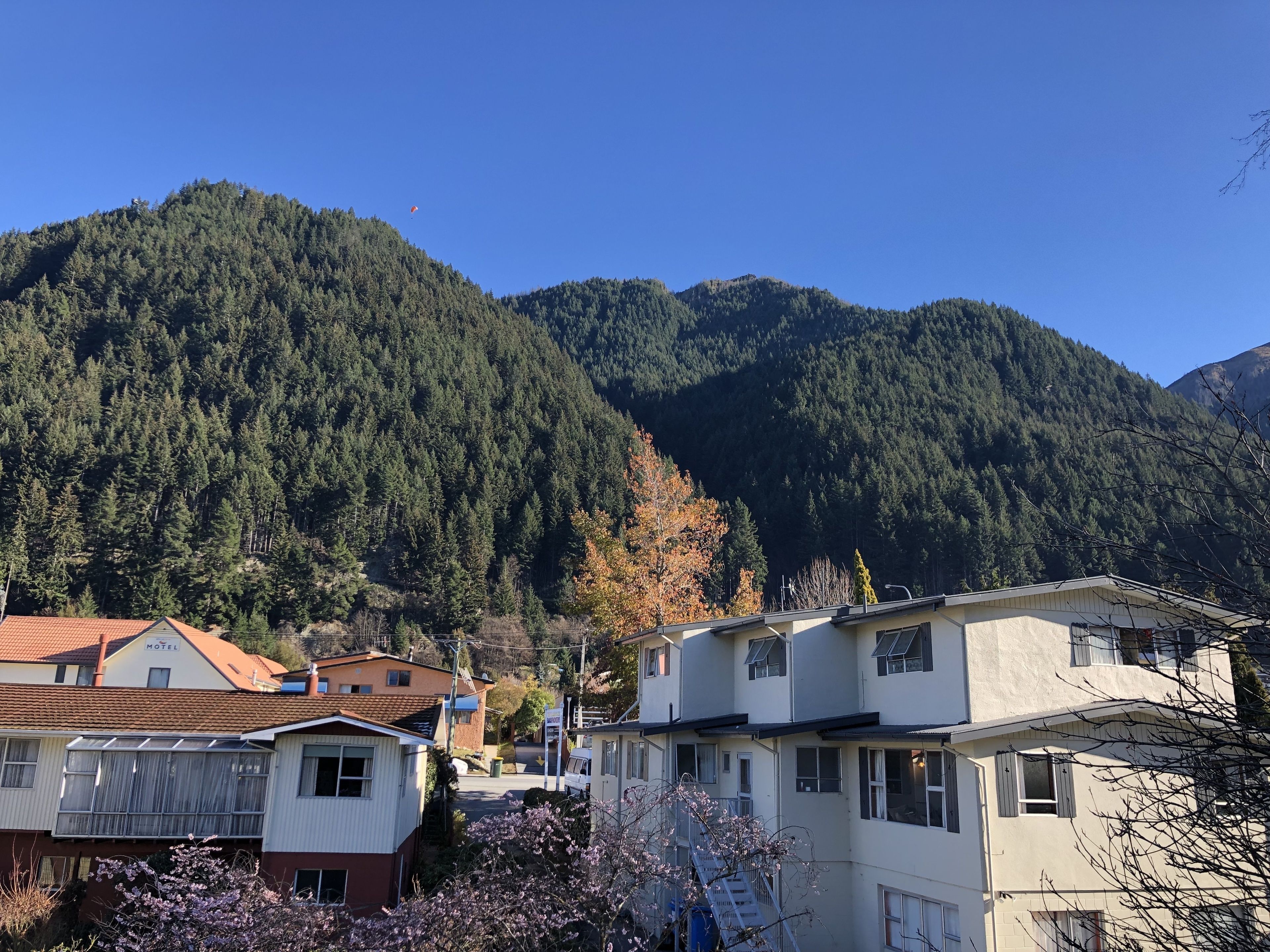 Un hôtel situé au pied d’une montagne, dont l’architecture combine des éléments modernes et traditionnels, avec une route bien visible et un ciel dégagé.