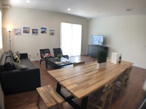Un salon moderne avec un canapé, une table basse et une table à manger. On y trouve également des œuvres d’art murales et un téléviseur posé sur un meuble.