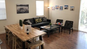 Ein modernes Wohnzimmer mit einem Holzesstisch, einem schwarzen Ledersofa und einem schwarzen Couchtisch. An den Wänden befinden sich mehrere gerahmte Bilder und auf dem Tisch steht ein Topfpflanze.